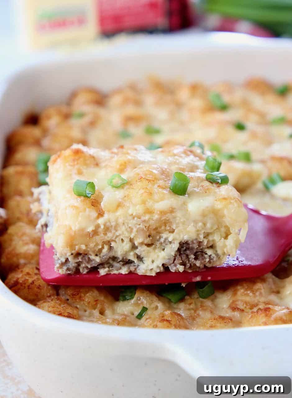 Slice of breakfast casserole on spatula coming out of the casserole dish. This easy, cheesy Tater Tot Breakfast Casserole is packed with flavorful eggs, sausage, and cheese, topped with crispy tater tots and more cheese, perfect for a make-ahead meal.