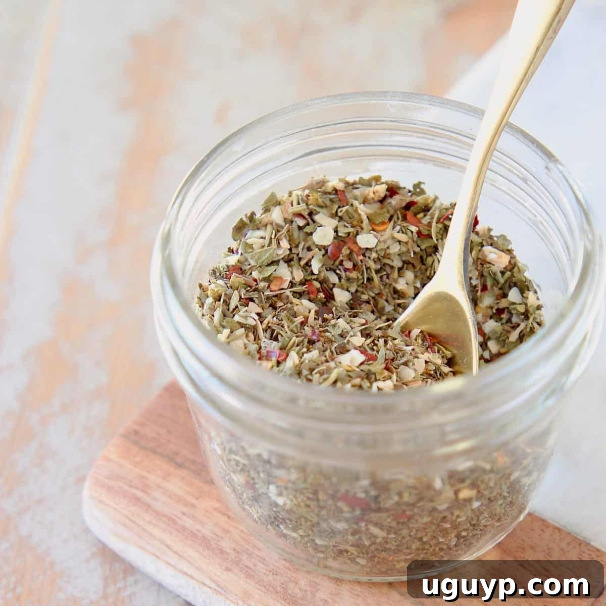 Mason jar of homemade Italian seasoning on a wood and marble cutting board with a small gold spoon in the jar. This easy homemade Italian Seasoning recipe is perfect for chicken marinades, seasoning vegetables, and enhancing pasta sauces, and is Whole30, vegan, and gluten-free.