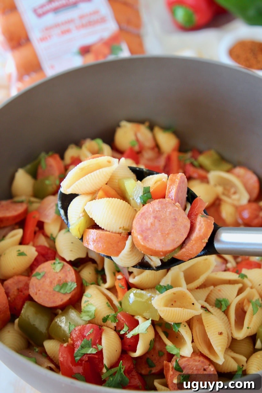 Cajun sausage and pasta in spoon, coming out of pot. This One Pot Cajun Pasta with sausage and peppers is an easy recipe made in just 29 minutes, cooked in a light and spicy tomato sauce for a scrumptious meal.