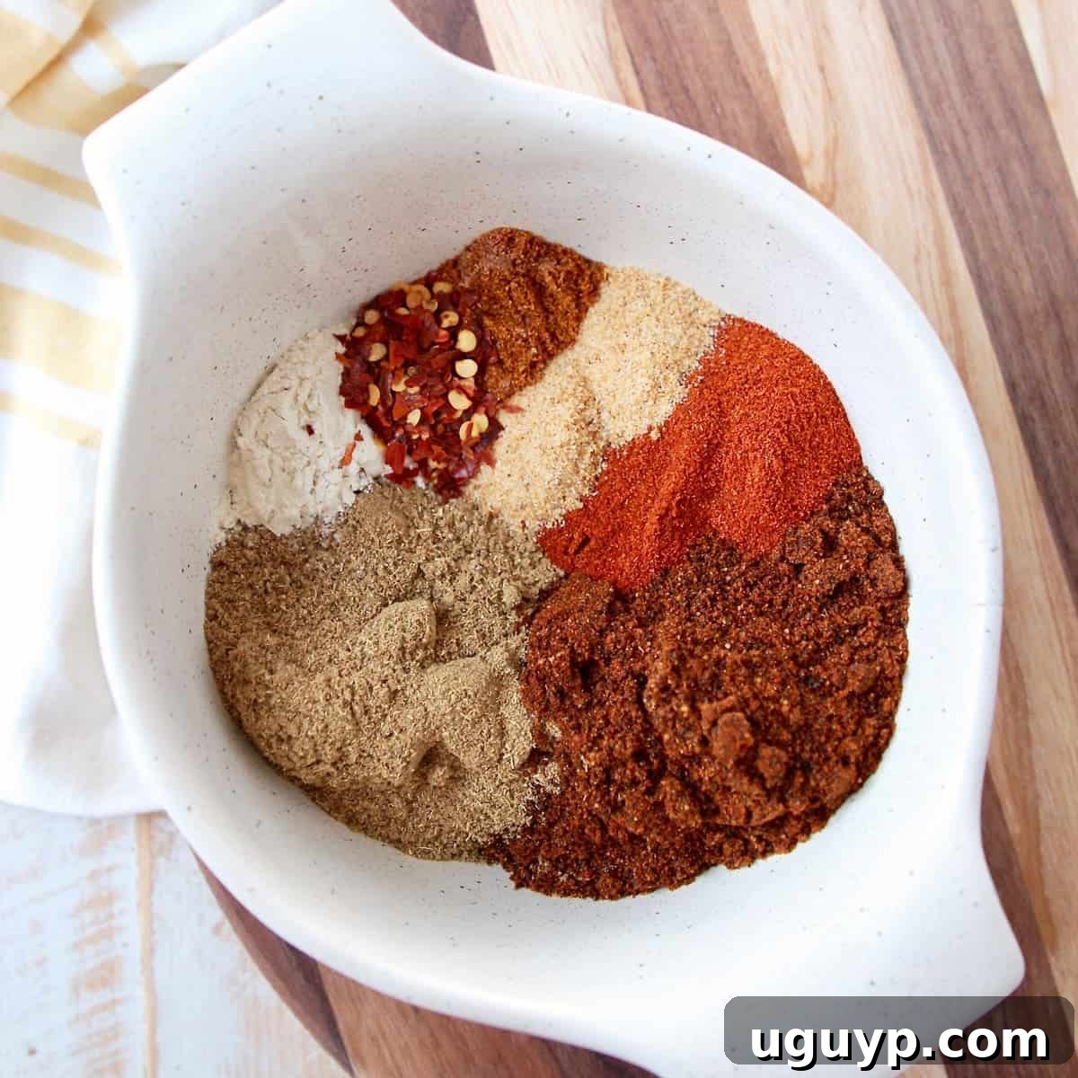 Eight spices for chili seasoning in a white bowl on a wood cutting board. This homemade Chili Seasoning mix is quick to prepare in under 5 minutes and is gluten-free, vegan, Whole30 compliant, and keto-friendly.