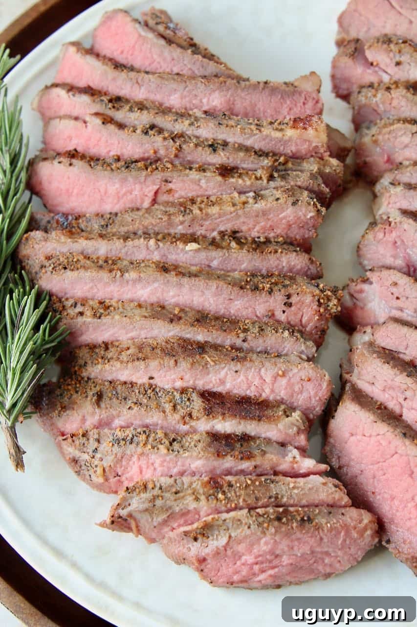 Sliced sous vide tri tip steak on plate with rosemary sprigs