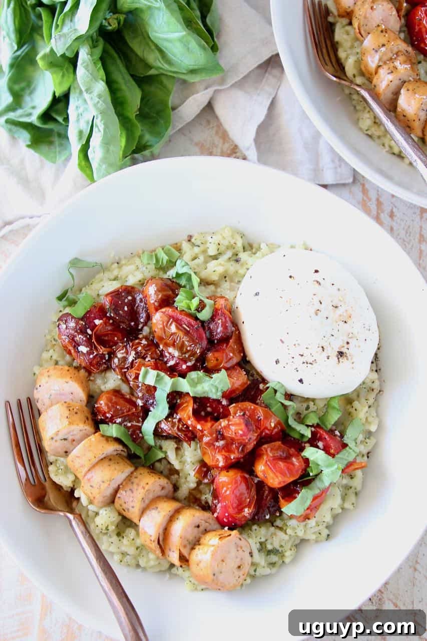 Creamy pesto risotto in a bowl, generously topped with sliced Italian sausage, vibrant roasted cherry tomatoes, and a dollop of creamy burrata cheese.