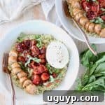 A top-down view of a bowl of creamy pesto risotto, adorned with roasted cherry tomatoes, slices of Italian sausage, and a pristine ball of burrata cheese, ready to be enjoyed.