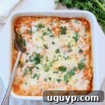 Cheesy buffalo chicken cauliflower casserole with a serving spoon, topped with fresh cilantro.