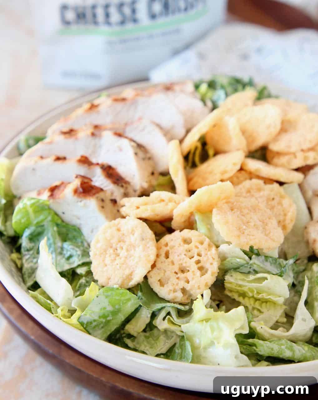 Close-up of Chicken Caesar Salad in a white bowl, generously topped with parmesan cheese crisps.