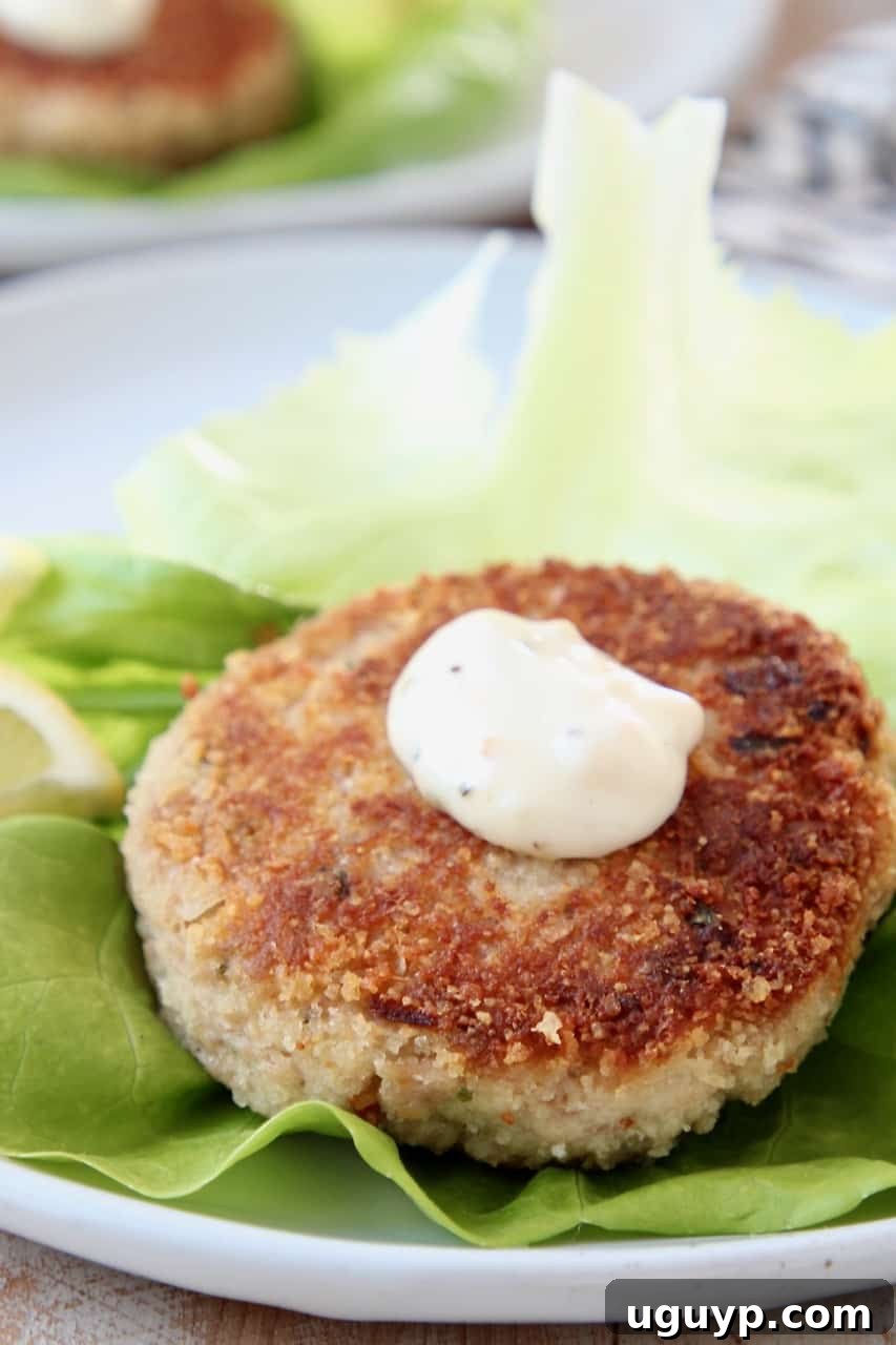A perfectly crispy tuna cake nestled on a fresh leaf of butter lettuce, elegantly topped with a dollop of creamy garlic aioli.