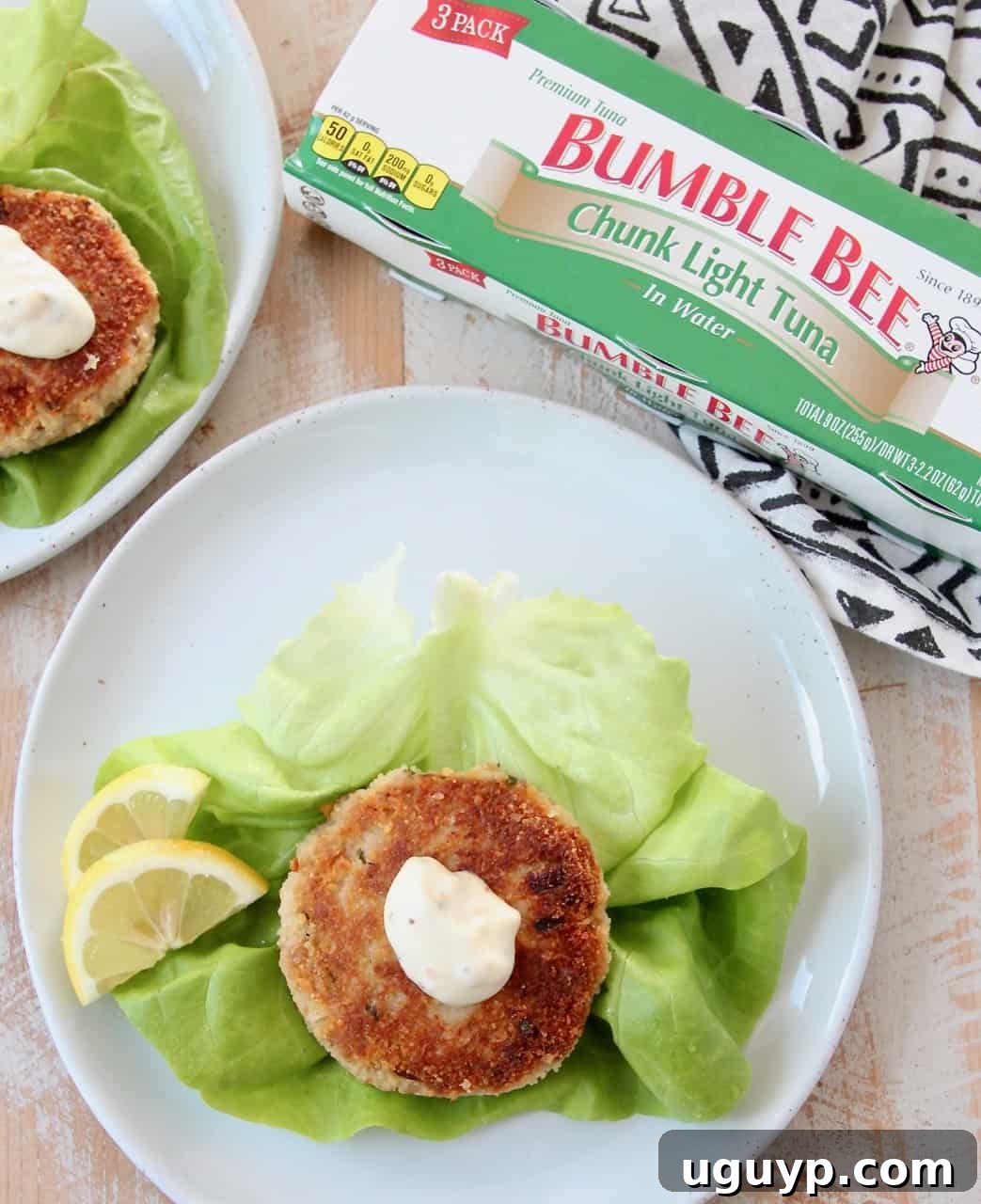 An overhead shot of a crispy tuna cake, artfully topped with a dollop of creamy aioli and fresh herbs, resting on a vibrant lettuce leaf.