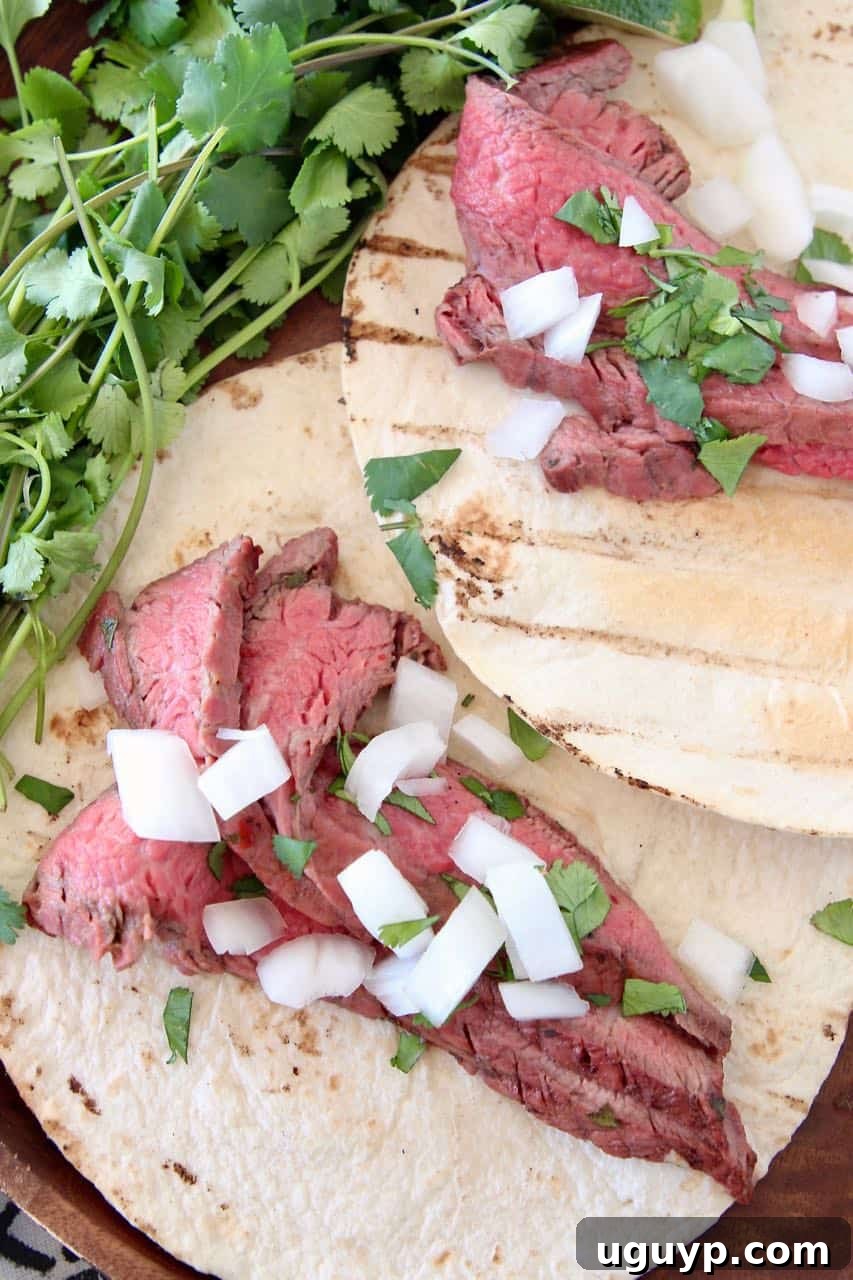 Sliced carne asada in tortillas topped with diced onions and cilantro, ready to be served