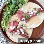 Two carne asada tacos on wood tray with fresh cilantro sprigs