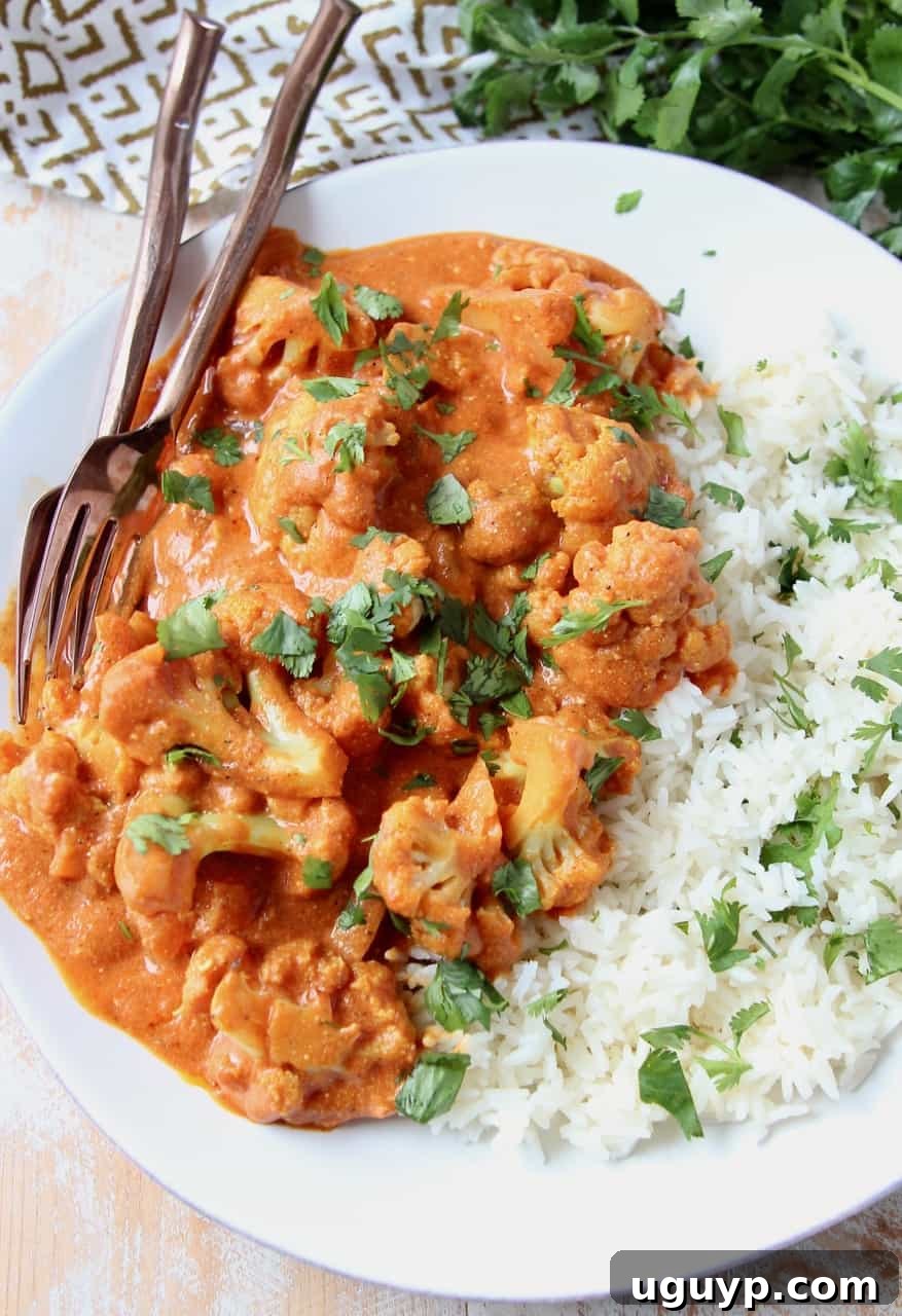 A plate of Indian Butter Cauliflower Curry served with basmati rice and fresh cilantro, with forks ready to enjoy.