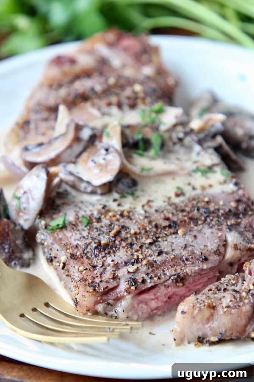 Perfectly sliced peppercorn steak on a plate with a fork, generously drizzled with creamy mushroom sauce, showcasing its juicy interior.