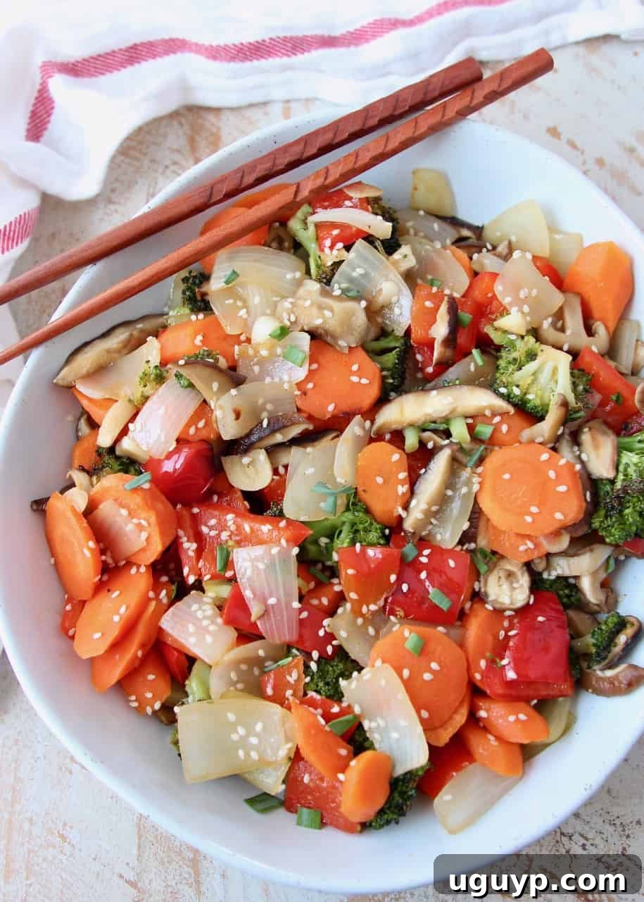 Overhead image of roasted Asian vegetables in a white bowl with chopsticks on the side, ready to eat