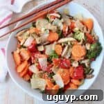 Overhead image of roasted Asian vegetables in white bowl with chopsticks on the side
