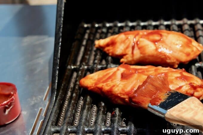 brushing bbq sauce on chicken on grill, creating a delicious glaze