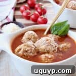Meatball soup in bowl with gold spoon and fresh basil leaves