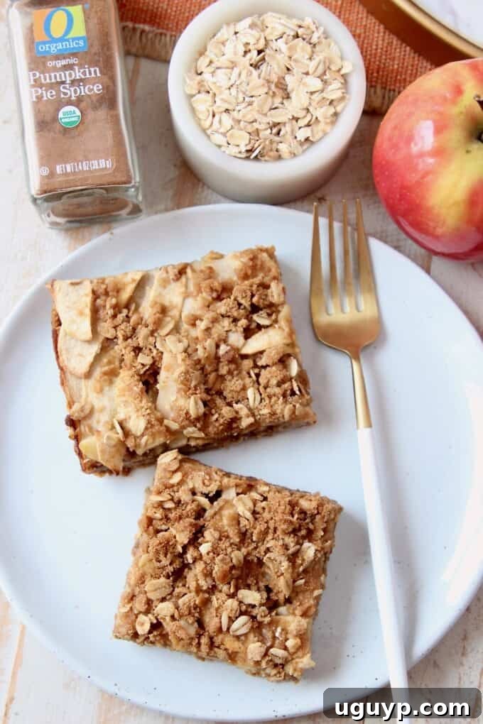 A close-up, overhead shot of a single pumpkin spice apple oatmeal bar on a simple white plate with a spoon, highlighting its inviting texture.