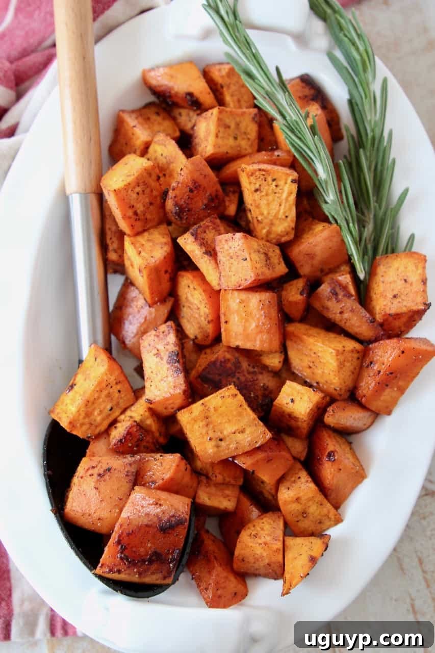 Roasted cubed sweet potatoes in a bowl with a serving spoon, garnished with fresh herbs