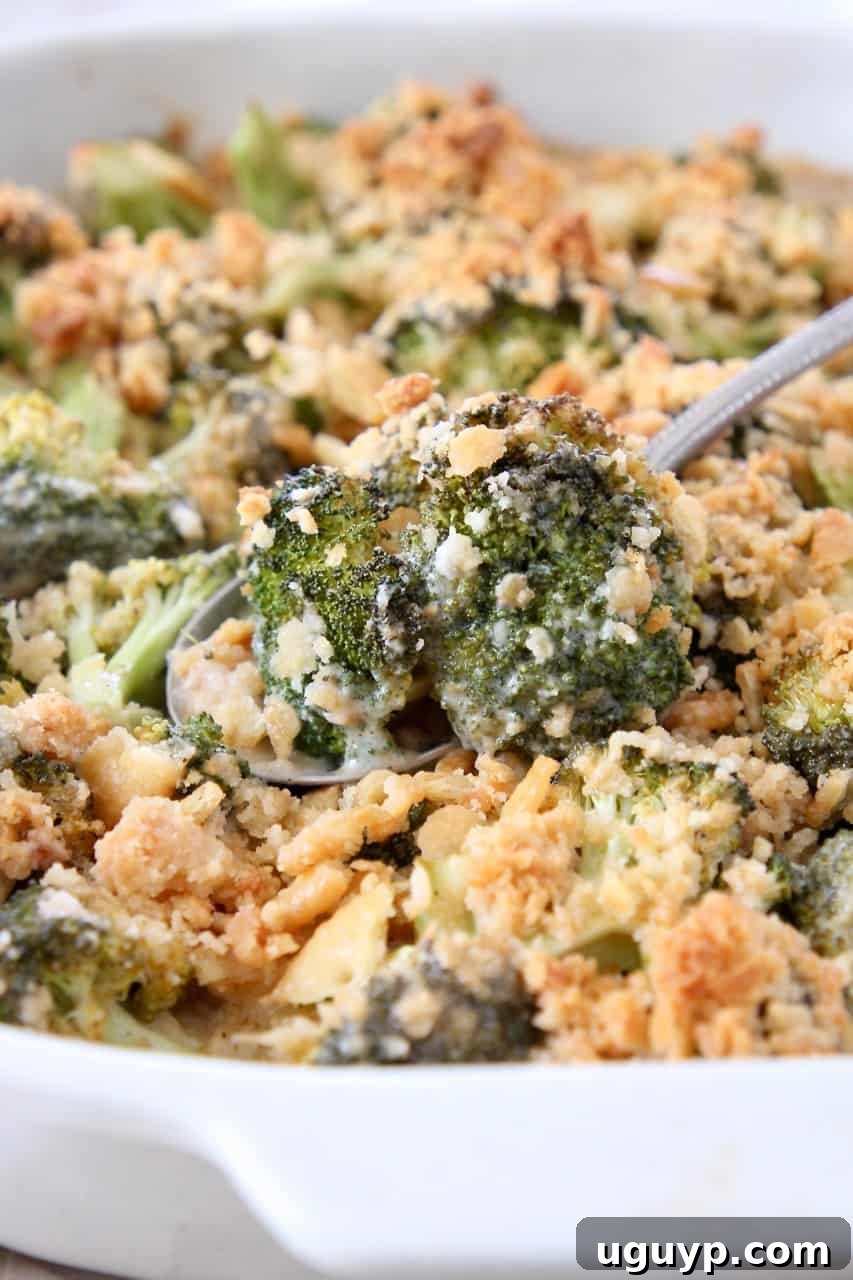 A serving spoon lifts a generous portion of cheesy broccoli casserole from the dish, showing its rich texture and topping.