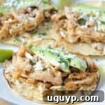 Shredded chicken tacos on plate topped with sliced avocado
