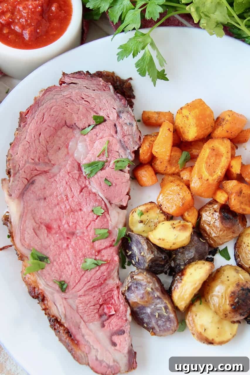 overhead image of sliced prime rib on plate with roasted vegetables, garnished with herbs