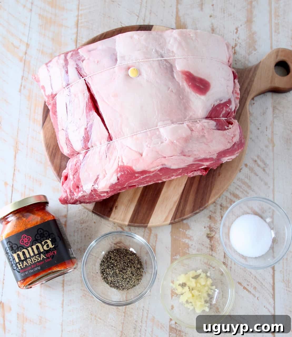 overhead image of ingredients for smoked prime rib, including bone-in roast, harissa, garlic, salt, and pepper