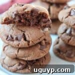 Close-up of a stack of richly dark chocolate cookies with visible chips, looking incredibly tempting.