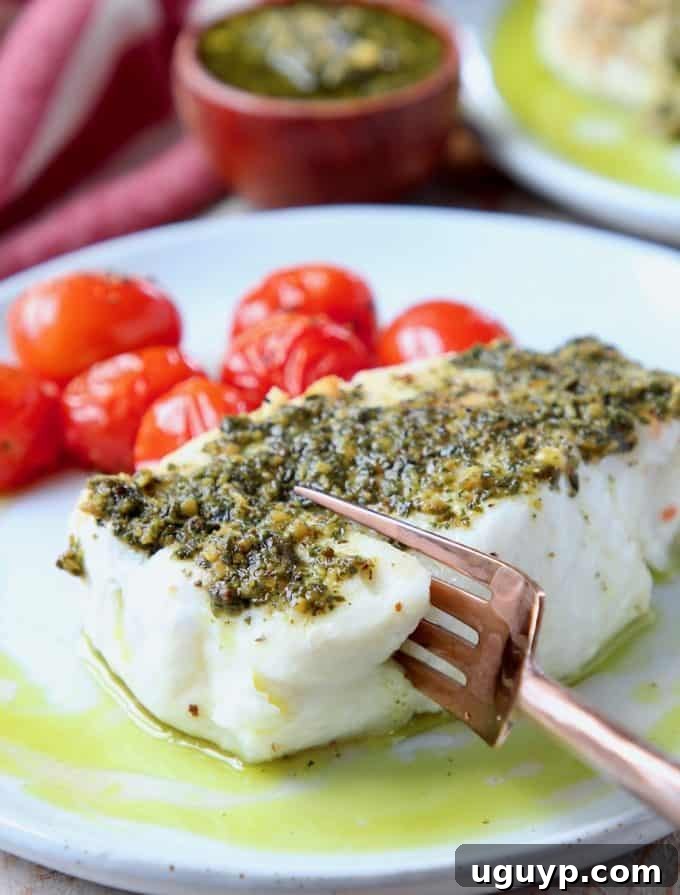 A fork gently cutting into a perfectly cooked fillet of Baked Chilean Sea Bass, elegantly plated and topped with fresh pesto, accompanied by a vibrant side dish, highlighting a healthy and gourmet meal.