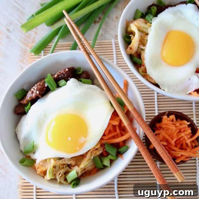 Two vibrant Korean BBQ Cauliflower Rice Bowls, each topped with a perfectly fried egg, shredded carrots, kimchi, and green onions, set against a rustic background, highlighting a healthy and flavorful meal option.