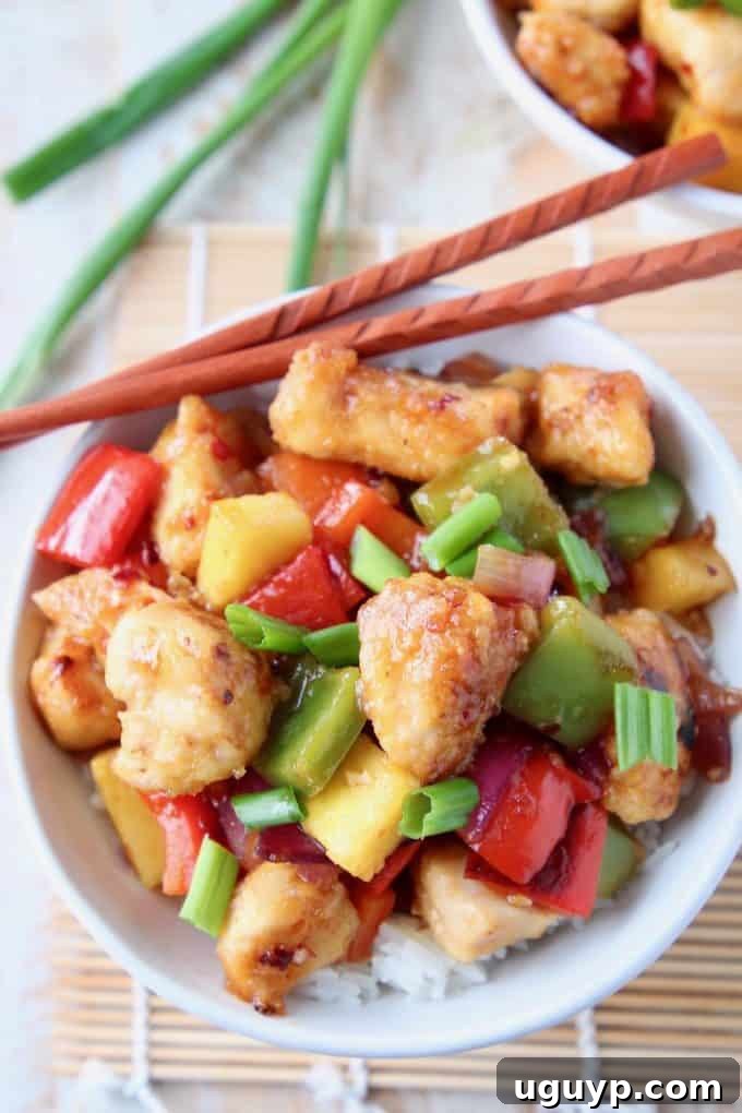 A vibrant bowl of Gluten Free Sweet & Sour Chicken, featuring succulent chicken, colorful bell peppers, and juicy pineapple pieces, garnished with fresh green onions and served with chopsticks, ready for a delicious Asian-inspired meal.