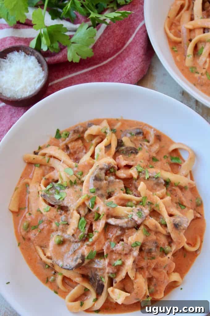 A close-up shot of a bowl filled with rich and creamy Pasta Boscaiola, featuring al dente pasta coated in a luxurious tomato-cream sauce with visible pieces of mushrooms and bacon, garnished with fresh parsley.