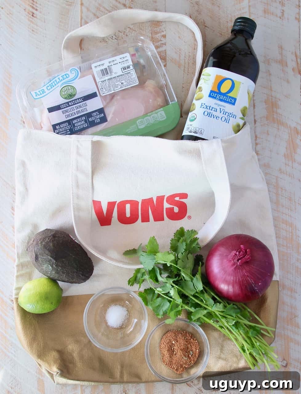 ingredients for guacamole stuffed chicken in a shopping bag on a white wood board