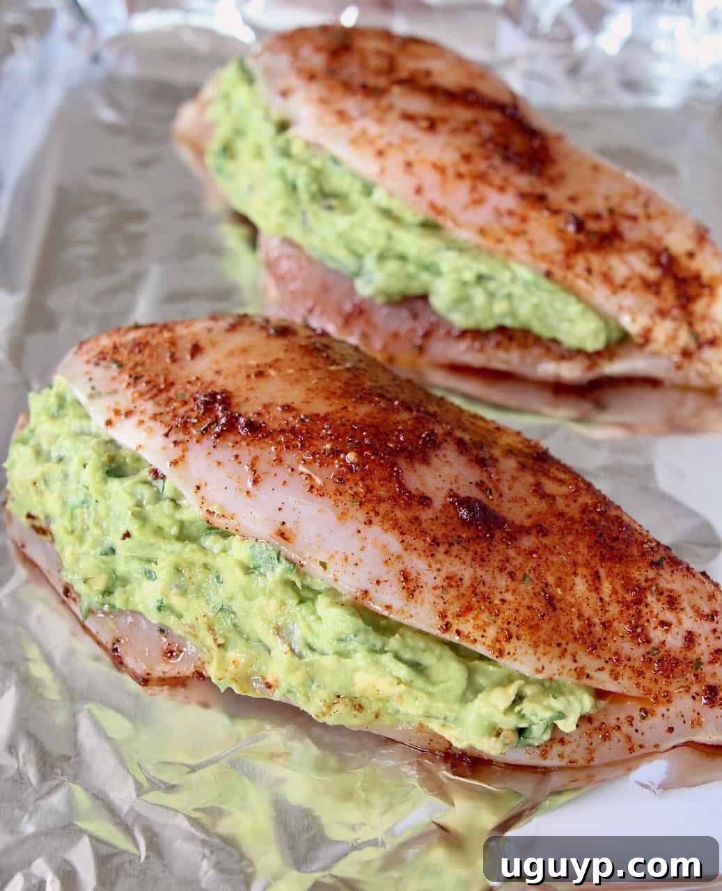 Uncooked guacamole stuffed seasoned chicken breasts on foil-lined baking sheet