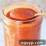 spoon of enchilada sauce lifted out of mason jar of sauce