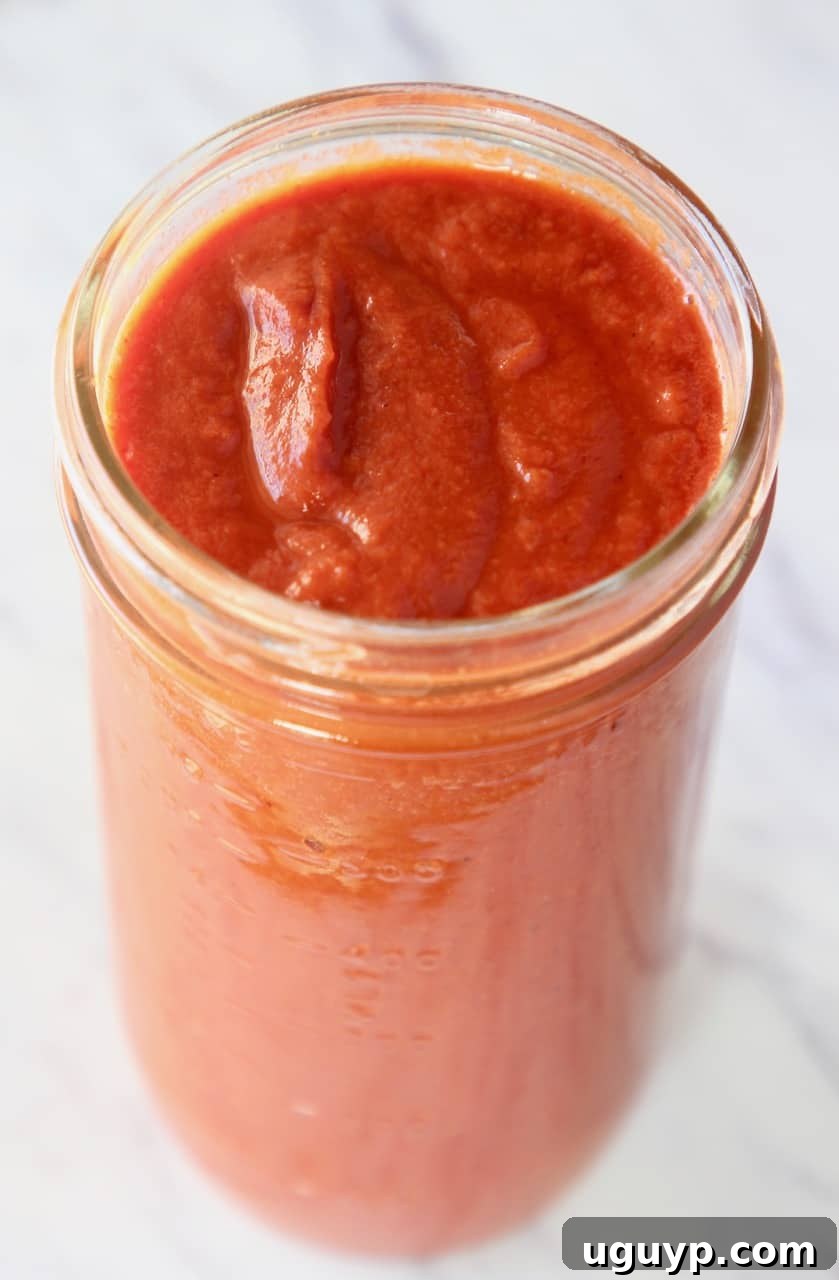 Tall mason jar filled with homemade red enchilada sauce, garnished with cilantro.