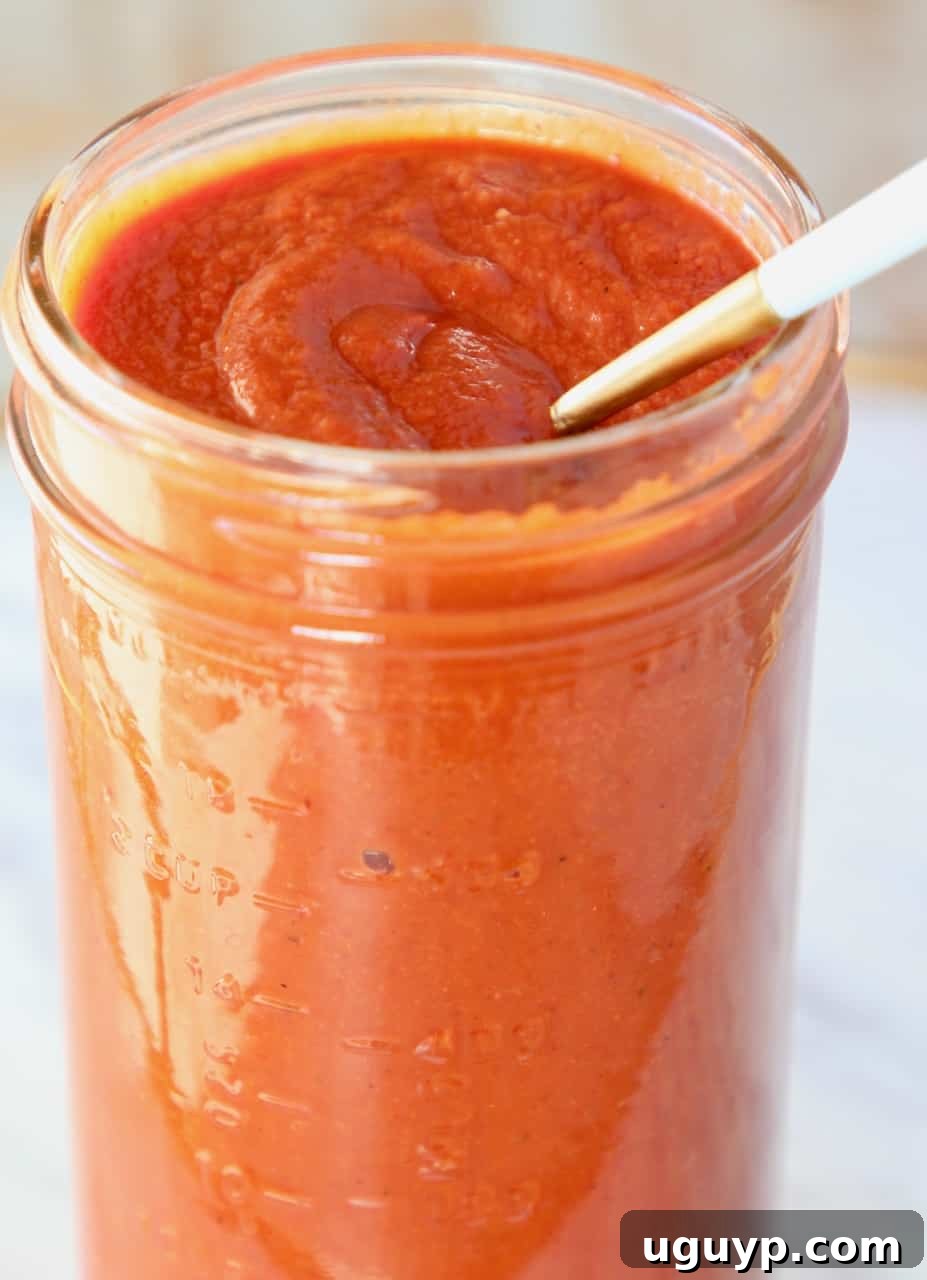 Close-up of a spoon in a mason jar filled with homemade red enchilada sauce, ready to use.