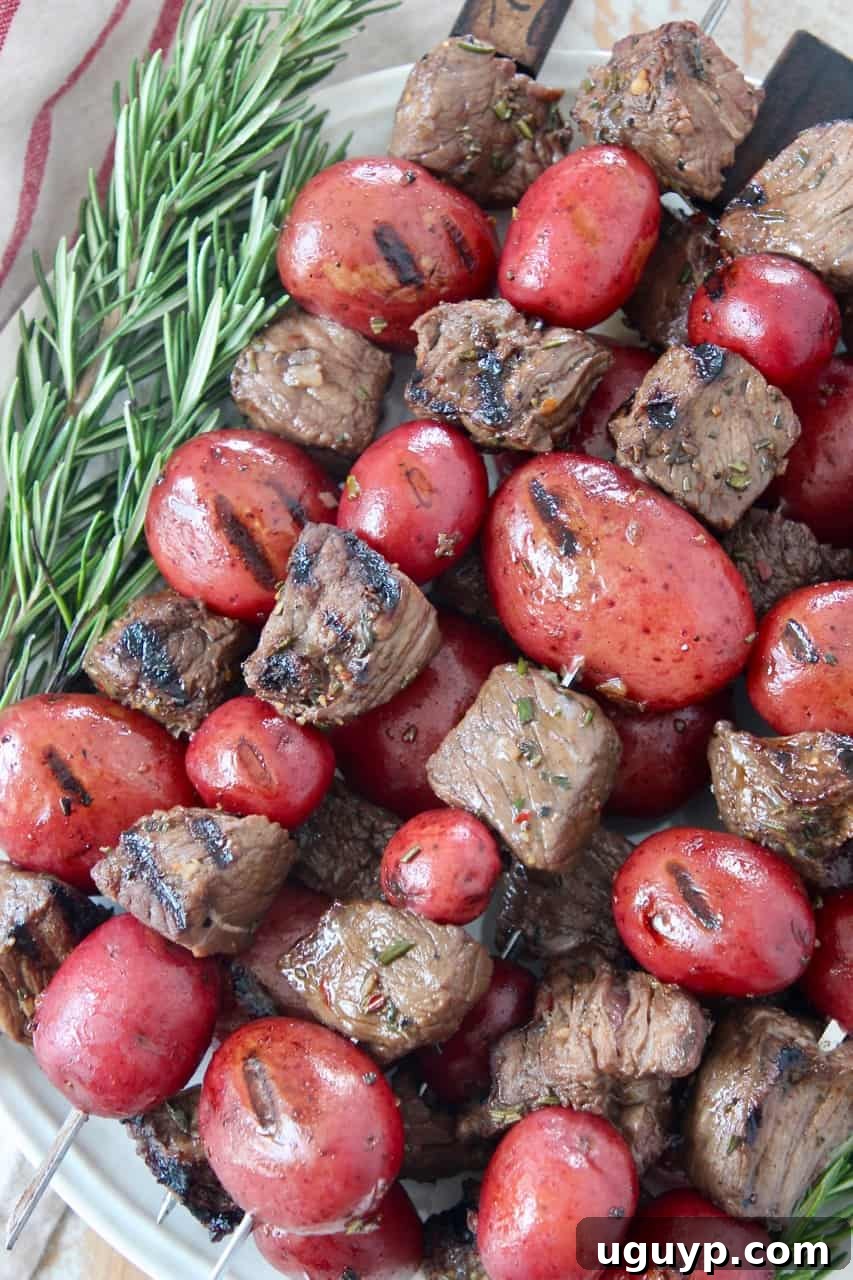 Pieces of steak and baby potatoes on skewers stacked up on a plate, seasoned to perfection.