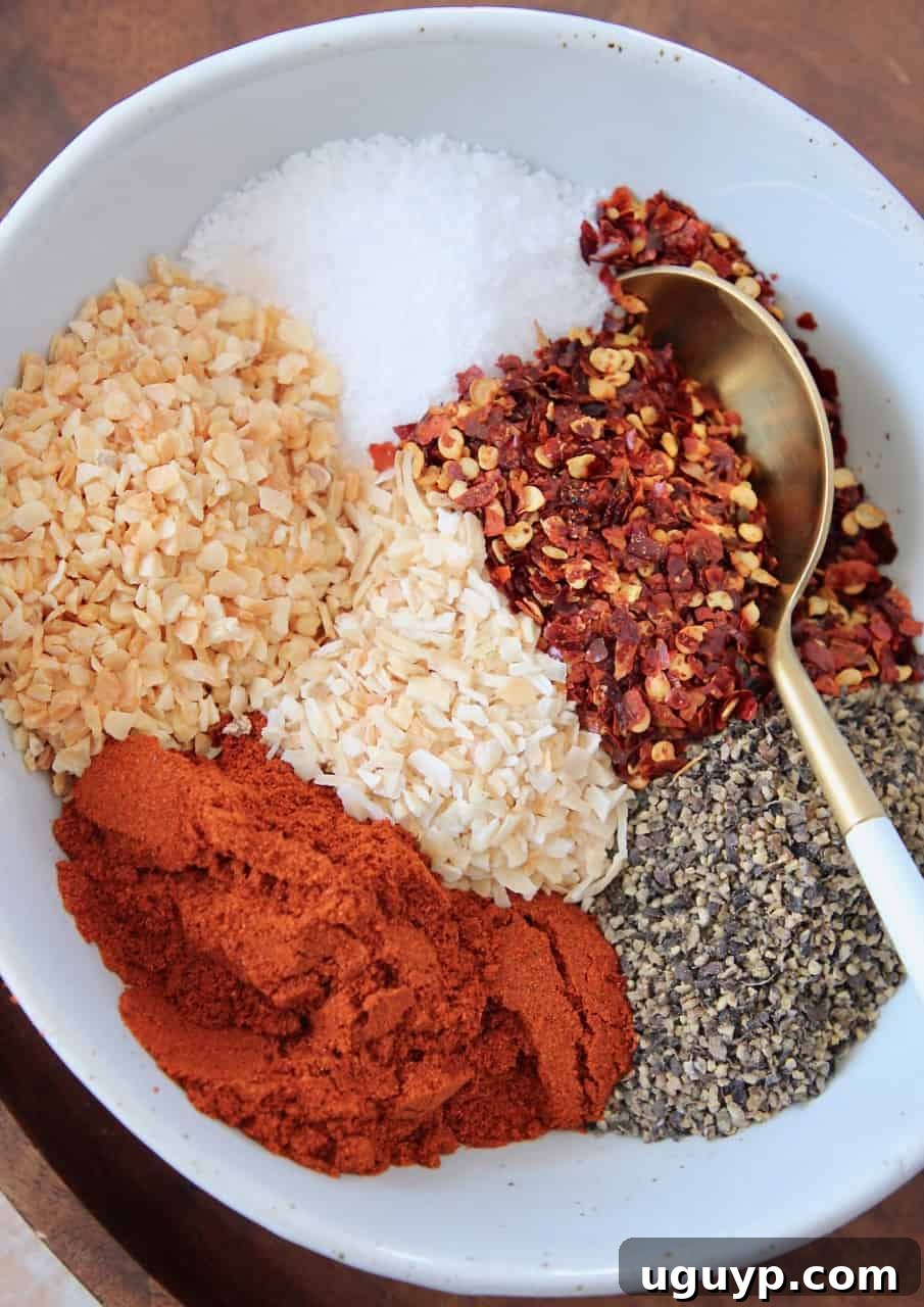 Overhead image of various coarse spices arranged in a white bowl with a spoon, highlighting the texture and blend.