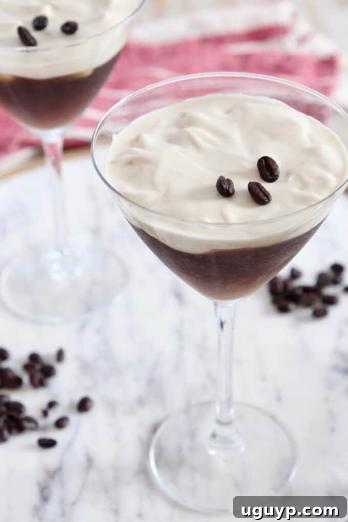 two espresso martinis in martini glasses sitting on marble serving tray, expertly garnished with whipped cream and coffee beans
