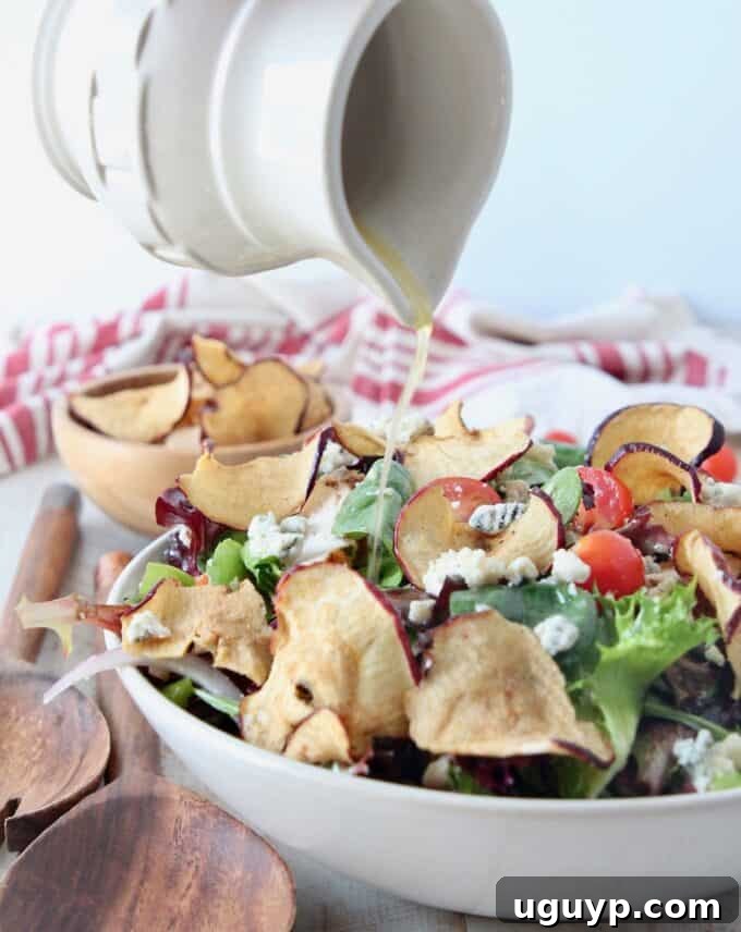 Small pitcher pouring homemade Fuji Apple Salad Dressing onto a fresh salad in a bowl, highlighting its vibrant color and smooth texture.