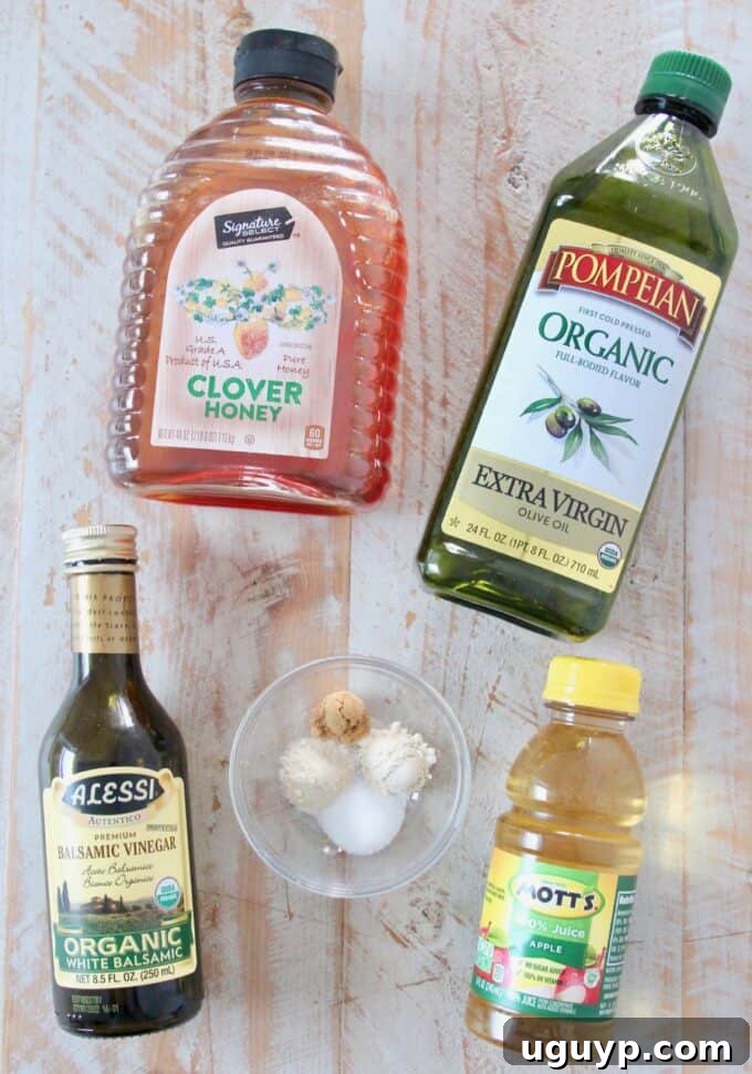 A flat lay photograph showcasing the individual ingredients for homemade Fuji Apple Salad Dressing: olive oil, white balsamic vinegar, honey, apple juice, sea salt, garlic powder, onion powder, and ground ginger.