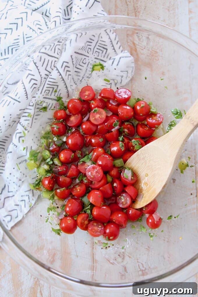 Halved grape tomatoes mixing with the aromatic lemon herb dressing in a clear bowl.