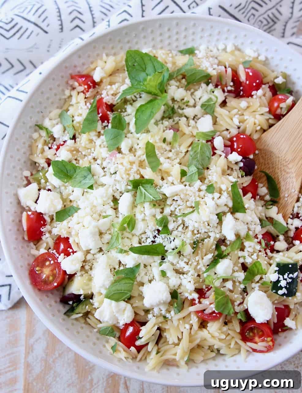 A beautiful bowl of Greek orzo salad, featuring vibrant tomatoes and creamy feta, with a wooden spoon.