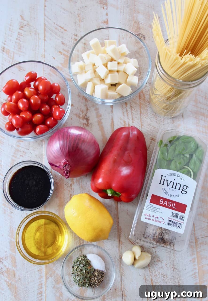 A colorful array of ingredients laid out for Caprese pasta, including angel hair pasta, grape tomatoes, fresh basil, red onion, bell pepper, garlic, mozzarella, olive oil, and balsamic vinegar.
