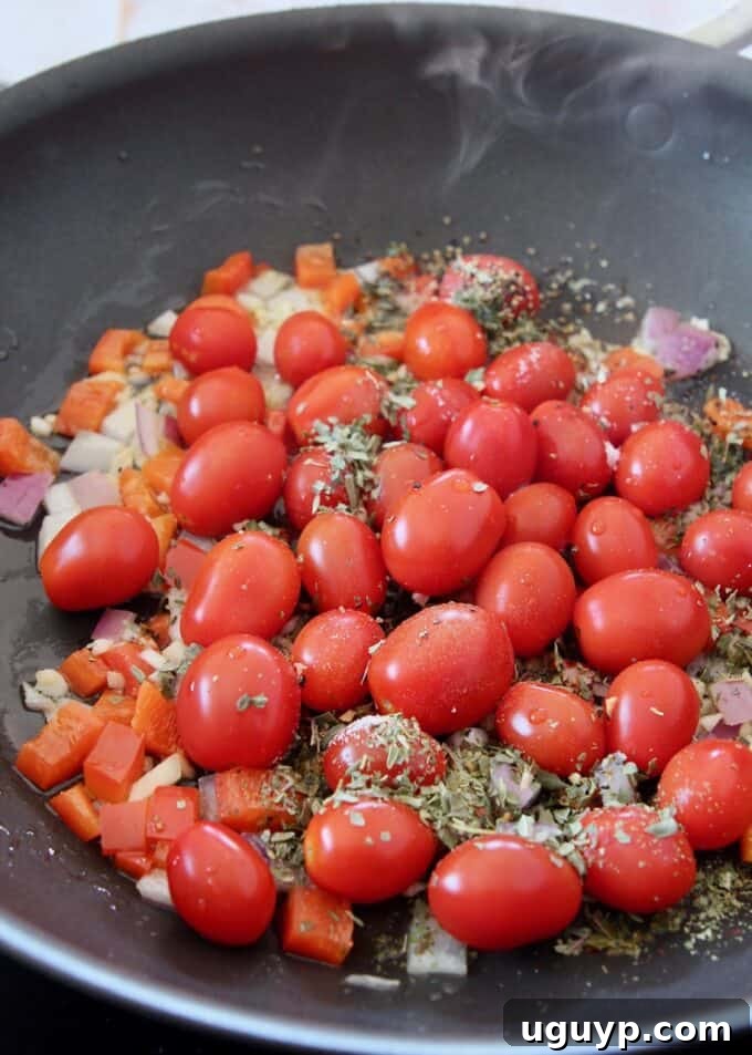Cherry tomatoes seasoned with Italian seasoning, lemon juice, salt, and pepper cooking in a large skillet, beginning to soften.