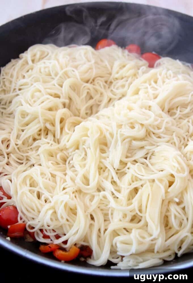 Cooked angel hair pasta added directly to the skillet with the tomato and vegetable mixture, ready to be tossed.