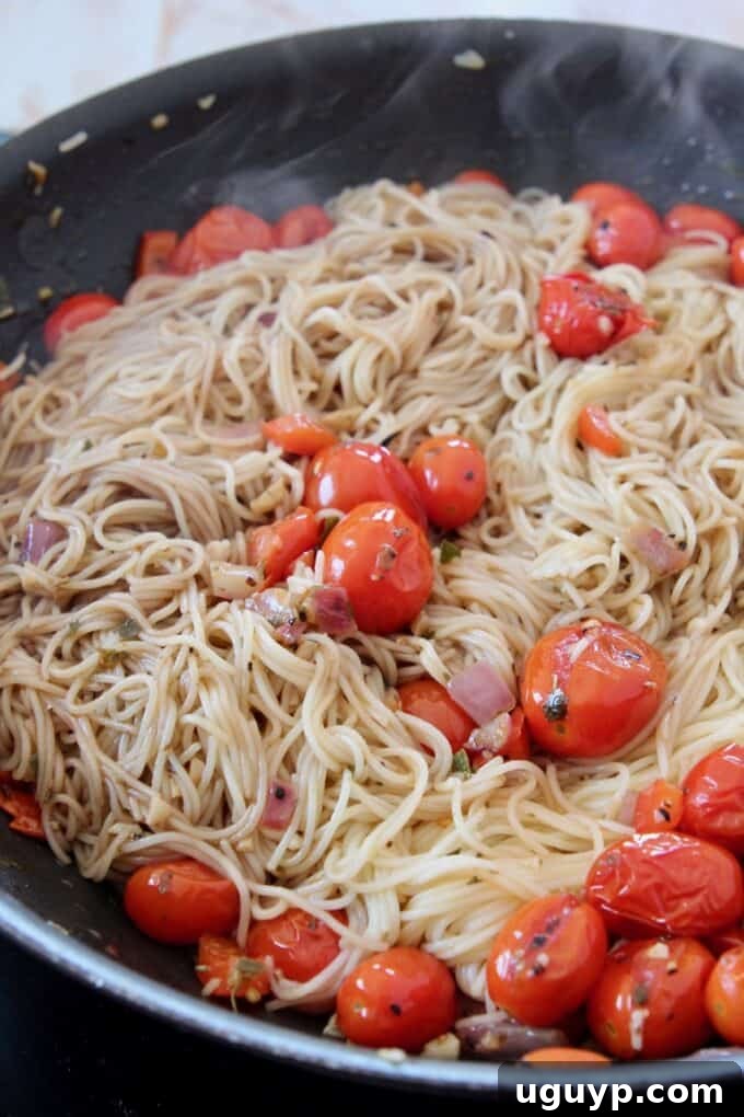 Angel hair pasta thoroughly tossed with the seasoned cherry tomatoes, onions, and peppers in the skillet, ensuring every strand is coated.