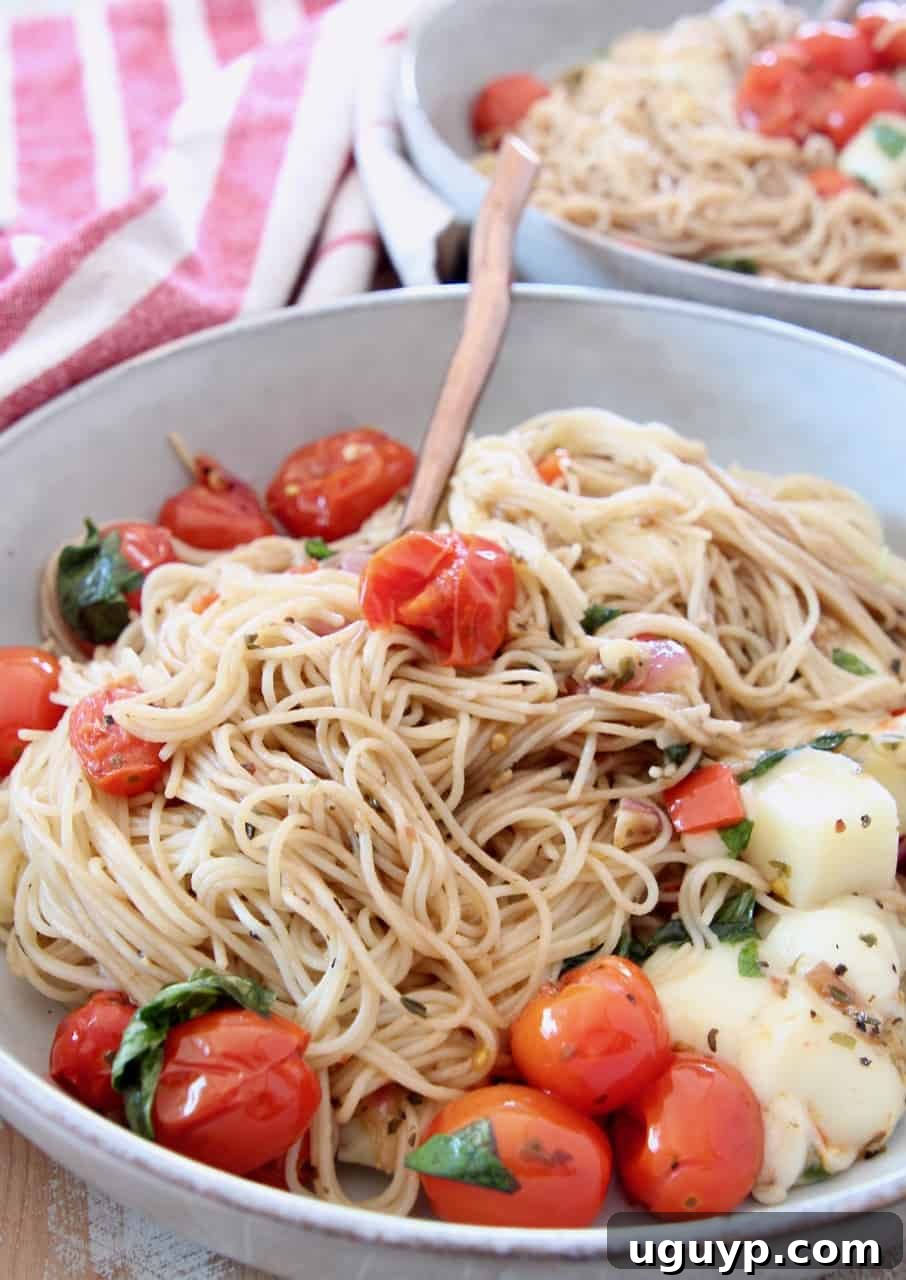 Close-up of Caprese pasta served in a bowl with a fork, showing the tender angel hair, colorful tomatoes, melted mozzarella, and fresh basil leaves.