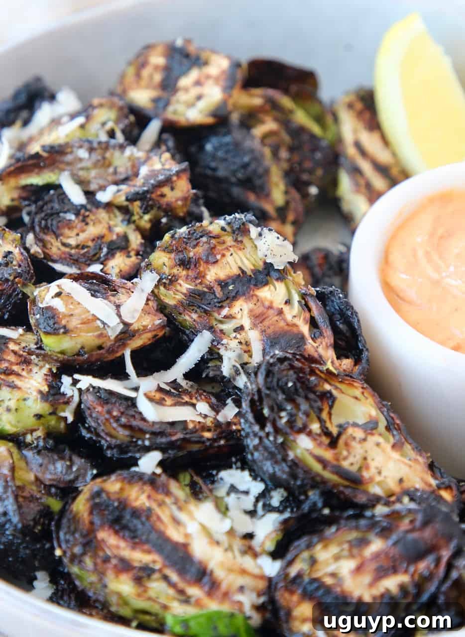 Grilled Brussels sprouts in a bowl with a lemon wedge and a side of harissa tahini sauce, showcasing their crispy texture.