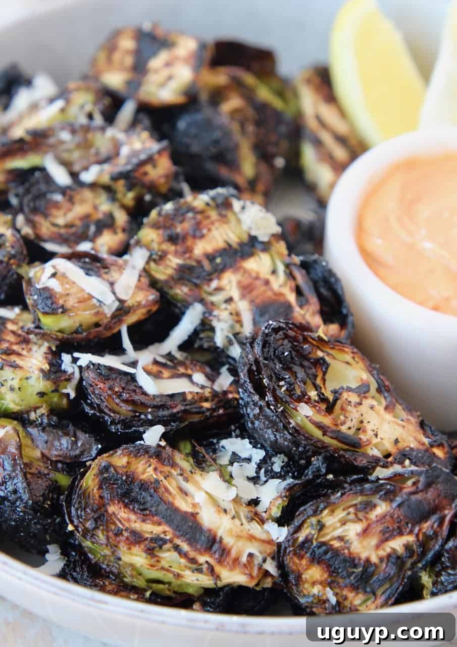 A bowl of easy grilled Brussels sprouts, perfectly charred and ready to be served with a delicious dipping sauce on the side.