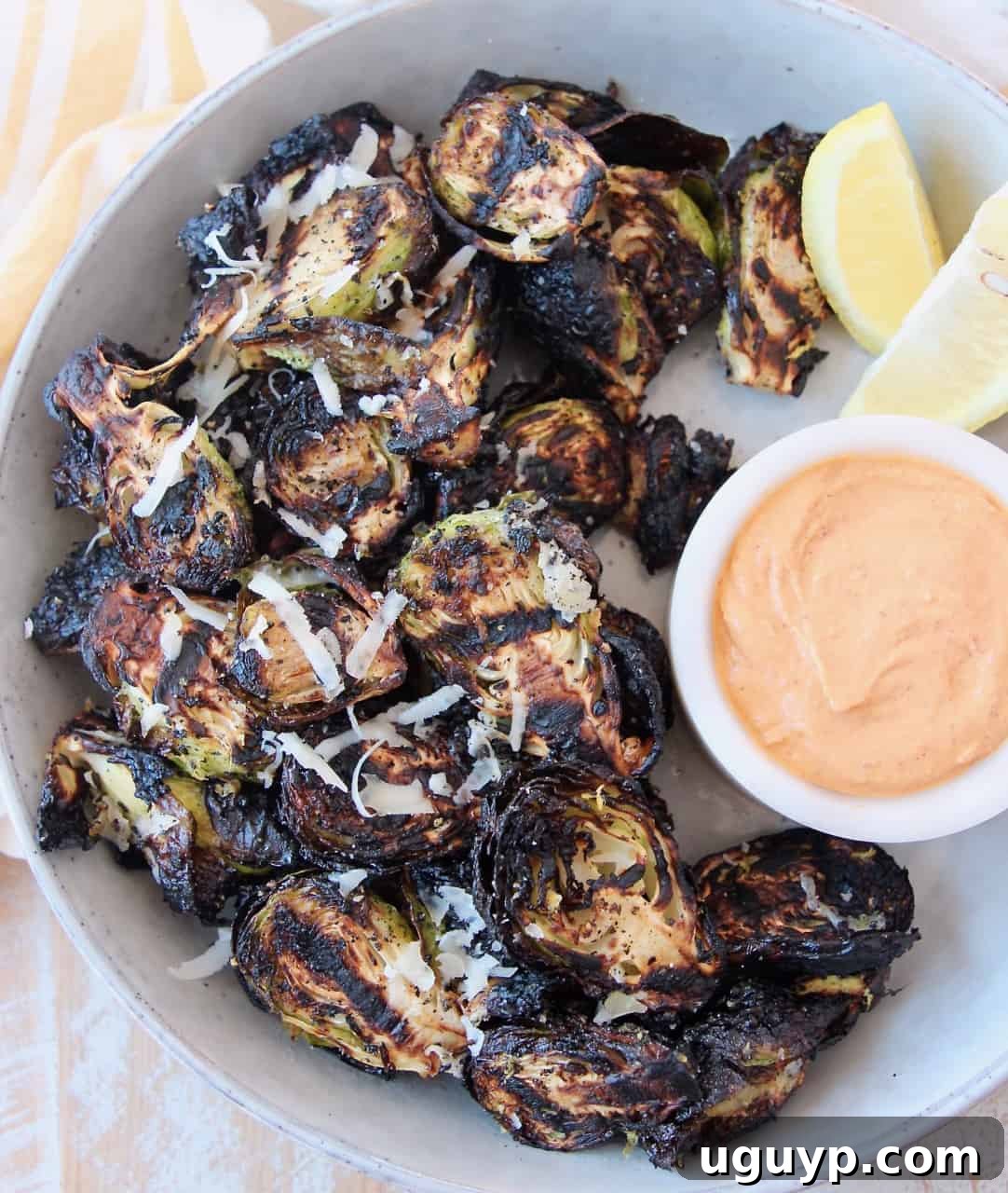 Grilled Brussels sprouts in a bowl, with a small dish of Harissa Tahini dipping sauce on the side.